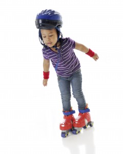 An adorable preschooler unsteady on her plastic roller blades. On a white background.